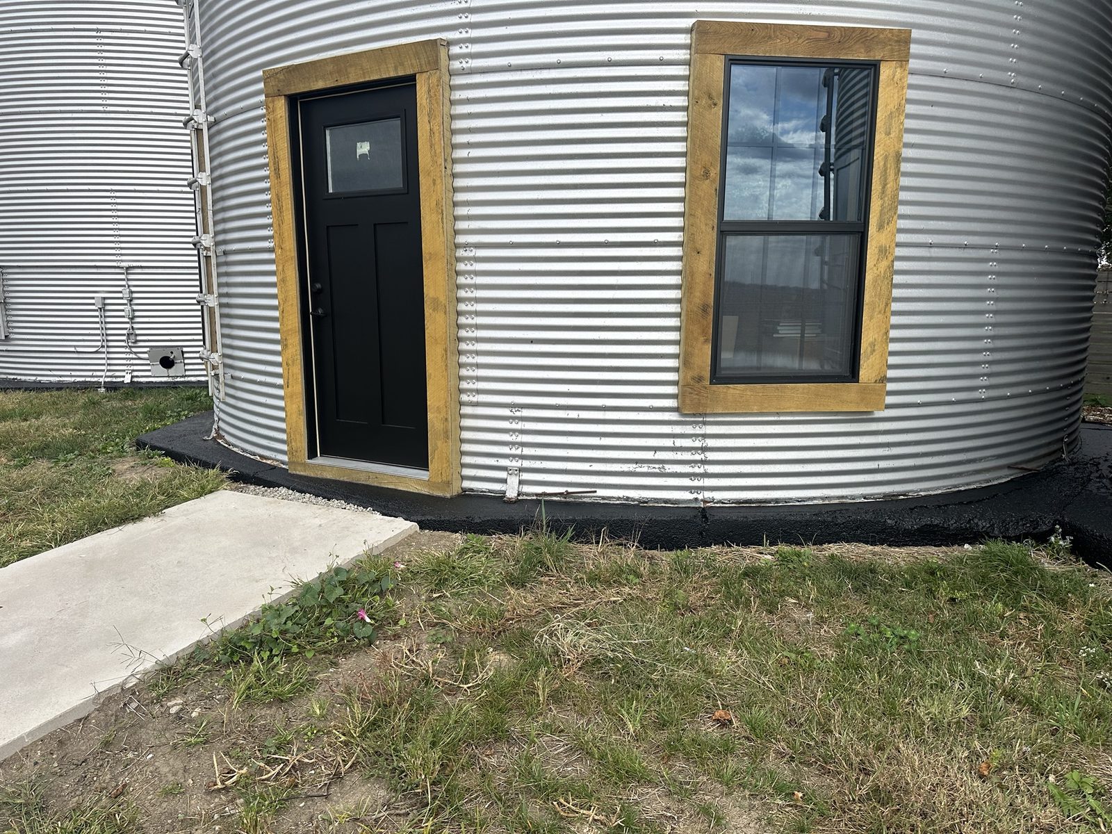 The same grain bin base after painting, with a clean black foundation band wrapping the corrugated metal