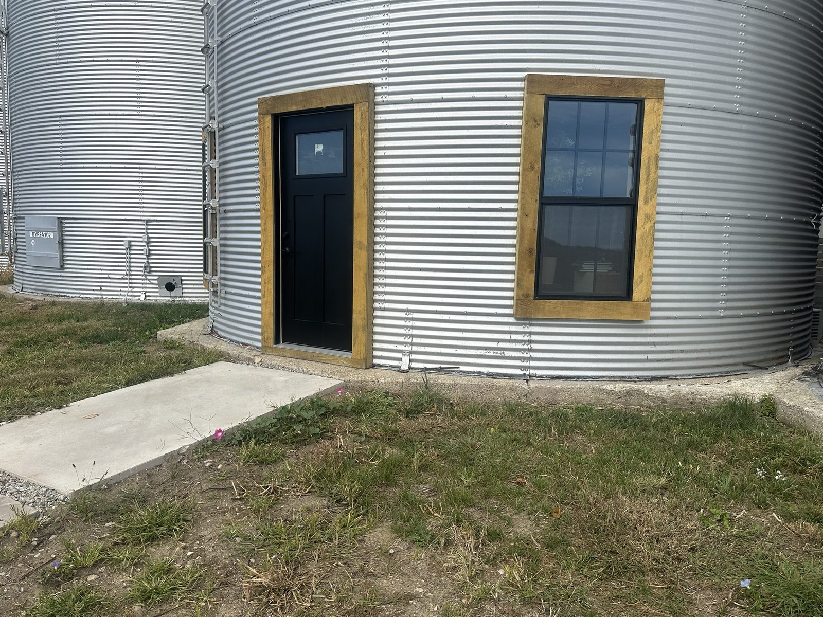 The base of a corrugated grain bin before painting, with bare concrete foundation showing at ground level