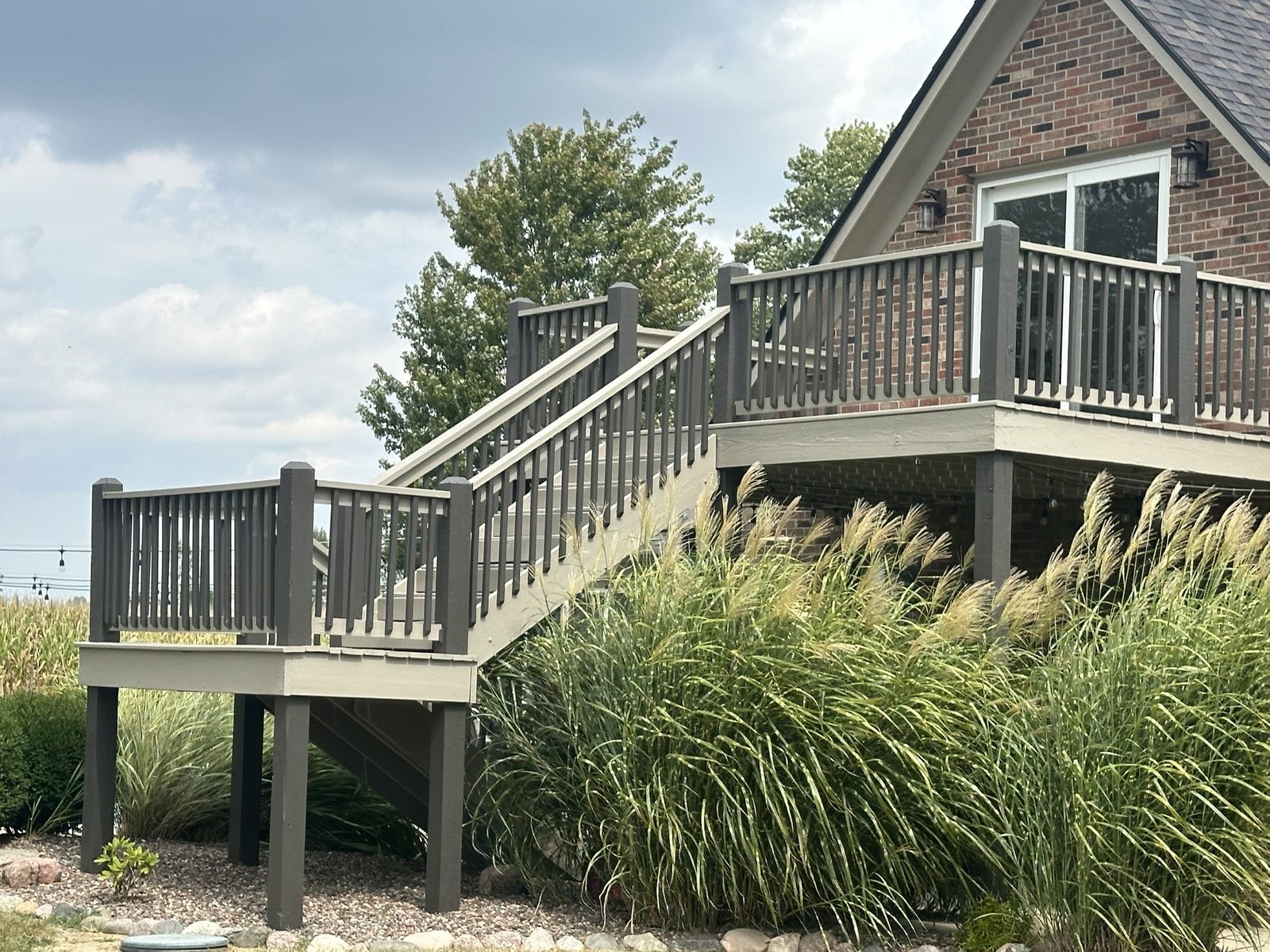 A stained deck and staircase on a brick home, dark rails with lighter treads and skirting