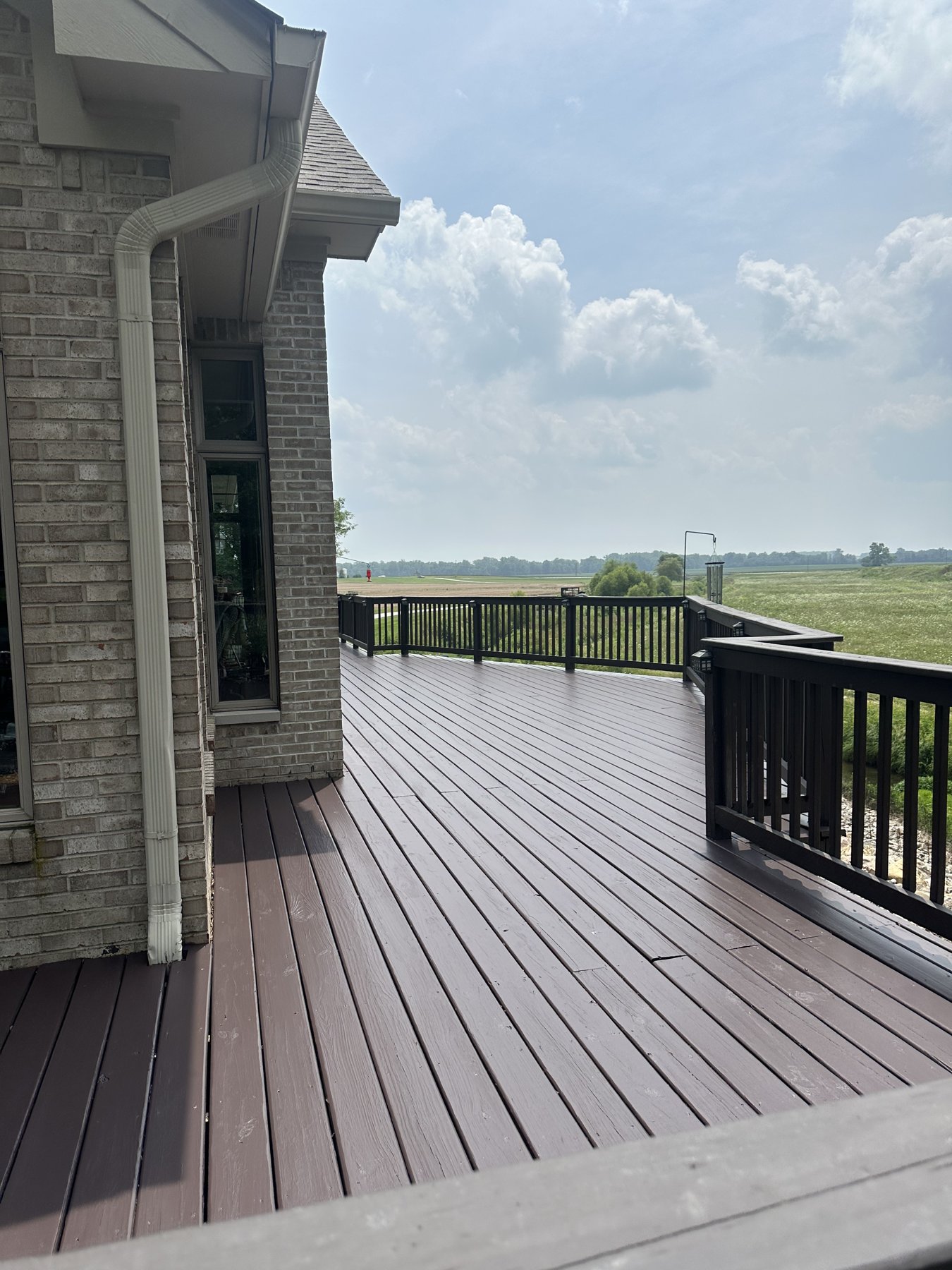 A freshly stained deck in rich brown with dark railings, overlooking open countryside