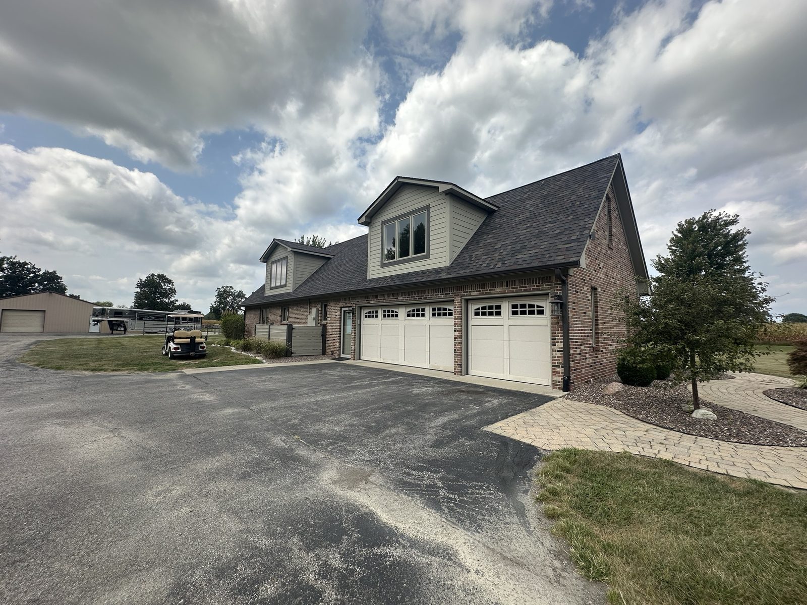A two-story brick home with sage-green dormer siding, matching trim and three white garage doors