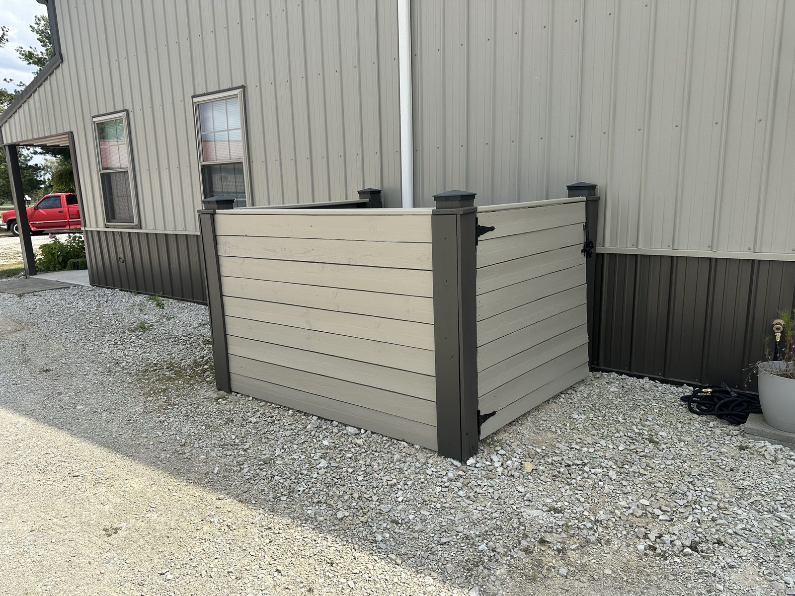 A tan horizontal slat enclosure with dark posts alongside a tan and brown pole barn