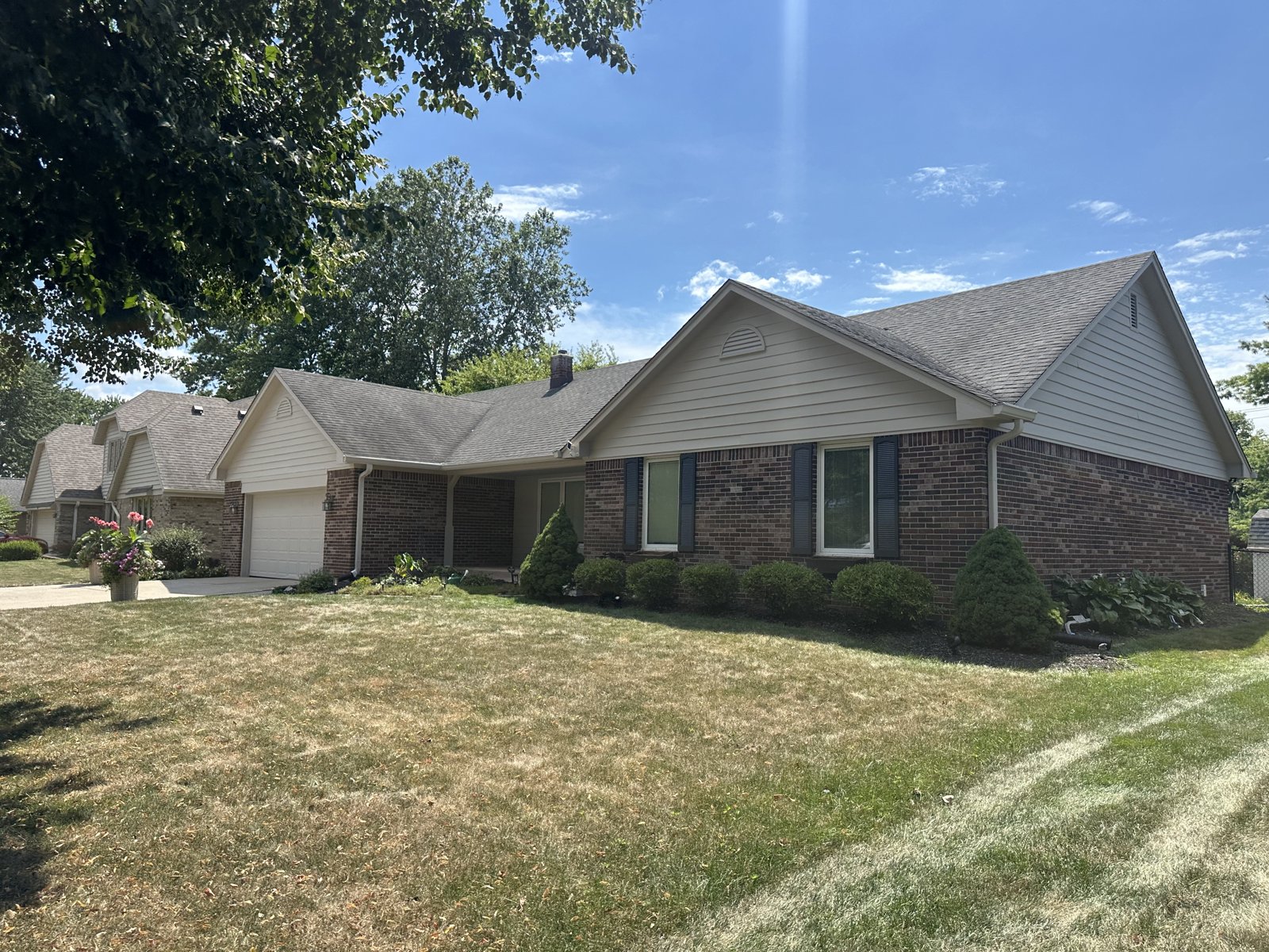 A brick ranch home with freshly painted tan siding, dark shutters and clean trim