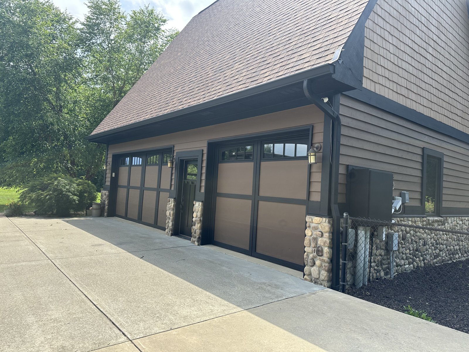 A home with tan siding, black carriage-style garage doors and stone accents, freshly painted