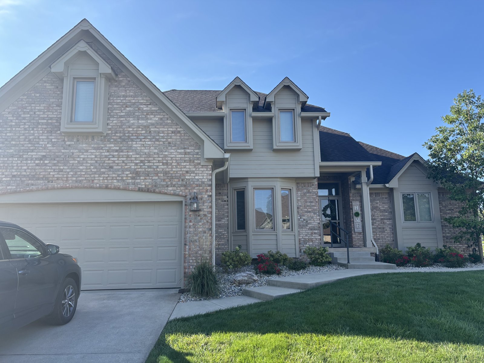 A two-story brick home with freshly painted tan siding, trim and dormers