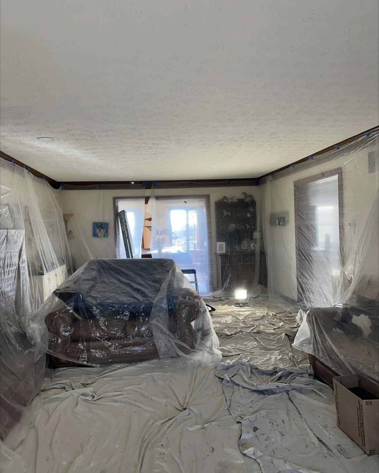 A living room with all furniture covered in plastic and floors fully draped before painting