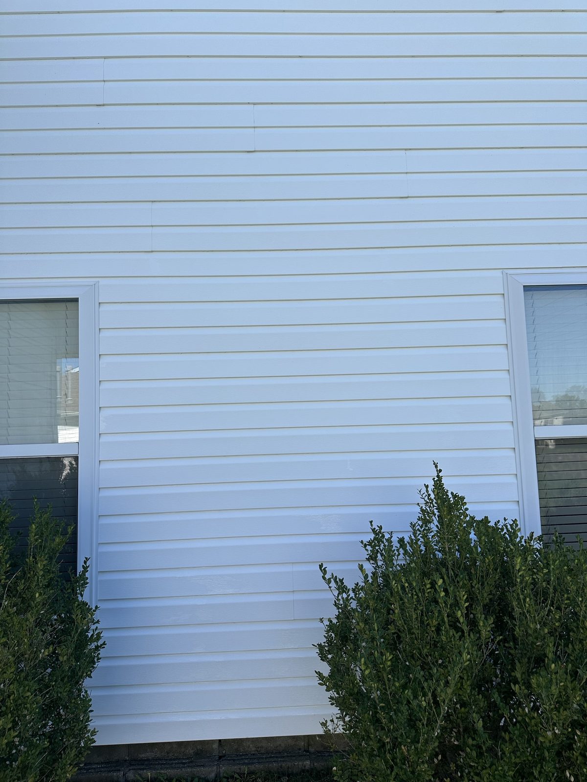 The same white lap siding after pressure washing, clean and bright with the staining gone